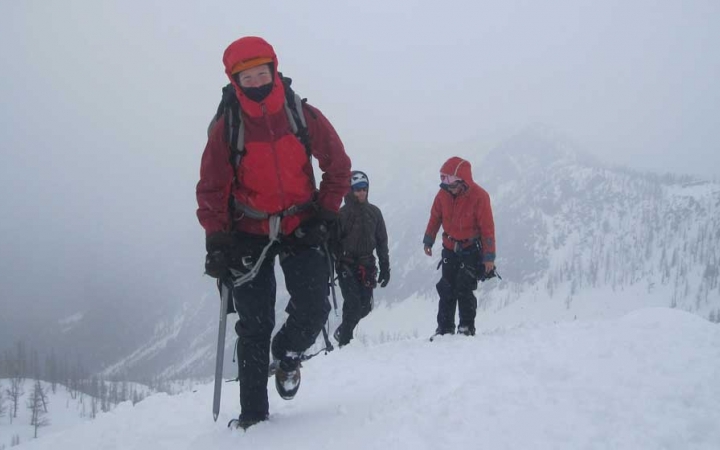 Three people in mountaineering gear make their way across a snowy, mountainous landscape.